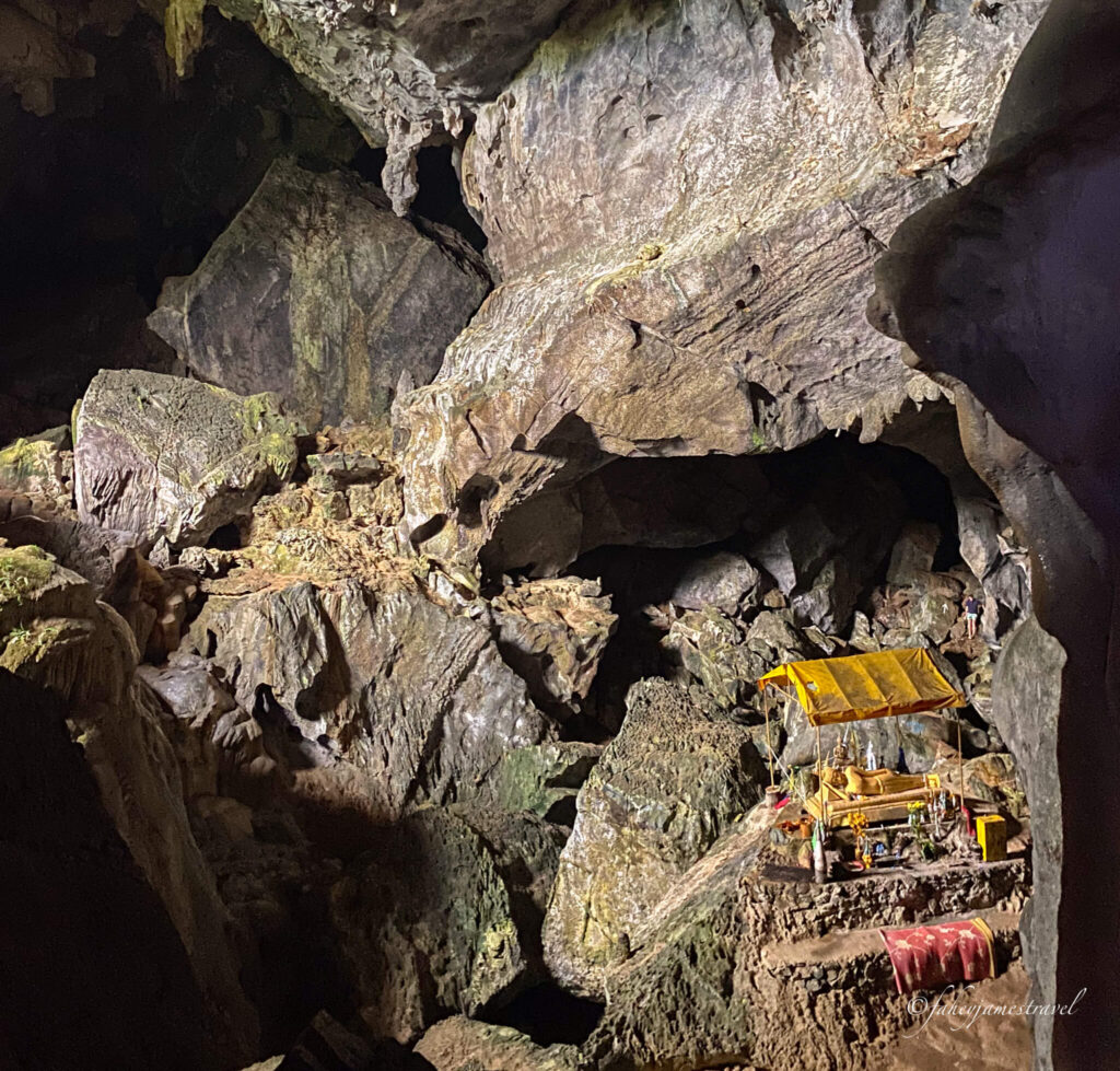 Inside Phu Kham Cave, there is a golden Buddha lying down under a yellow cover. The cave is huge, and dark colours are shown