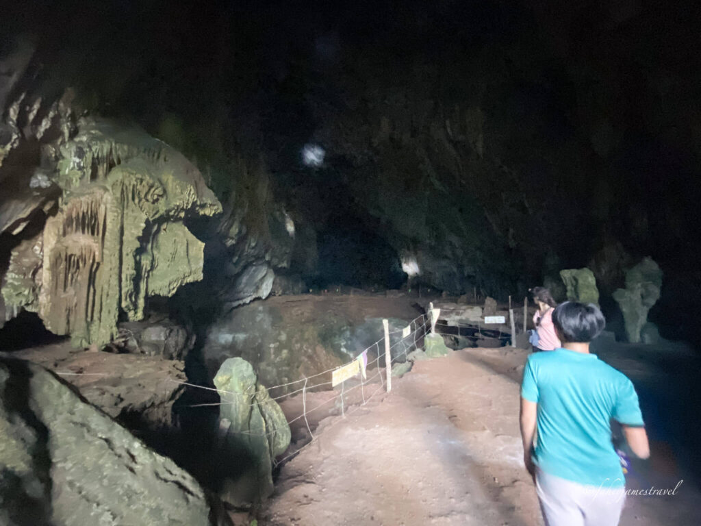 guide and tour guide walk through the big open cave, where it gets darker in the background