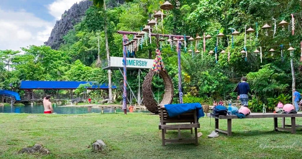 Swimming is shown at Blue Lagoon 2, and the grass is very green as people stand in the water, and some people swim. There is a beach to leave your clothes on the front