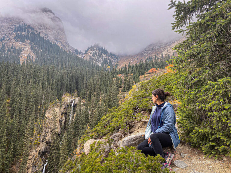 guads sites and looks out over the big drop to barskon waterfall in the background. she looks over her shoulder and sees the cloud and trees