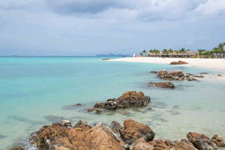 north point beach on koh lipe. some rocks are i the fore and middle ground and the sky is cloudy with blue clear water