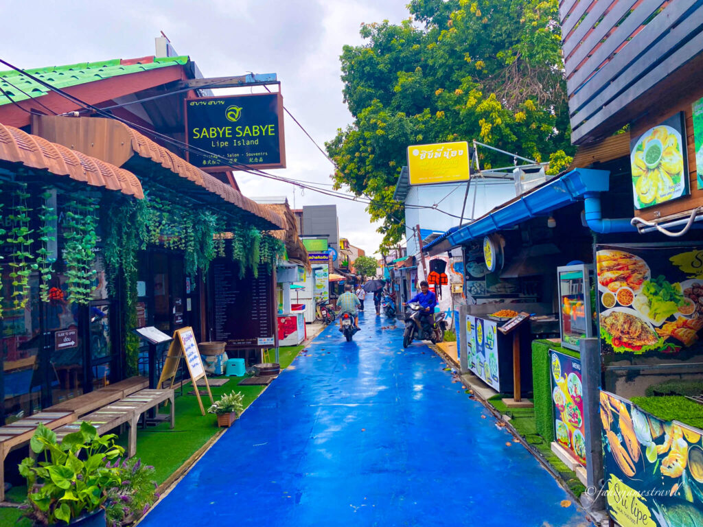 walking street is blue and there is one motorbike moving through the street. few people to be seen.