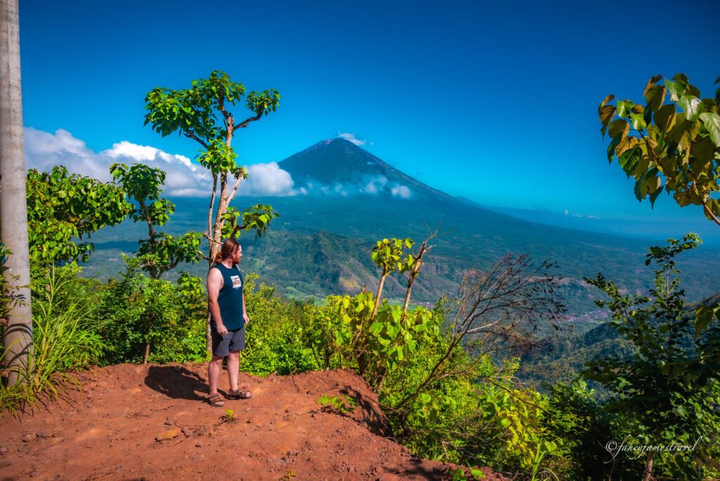 james stands beside the cliff on the walk up to lahang sweet near amed bali. mount agung is standing tall in the background 