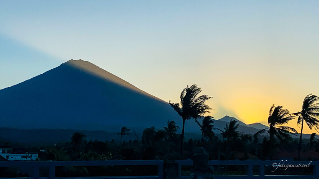 a beautiful light shines over mount agung and palm trees are blowing 
