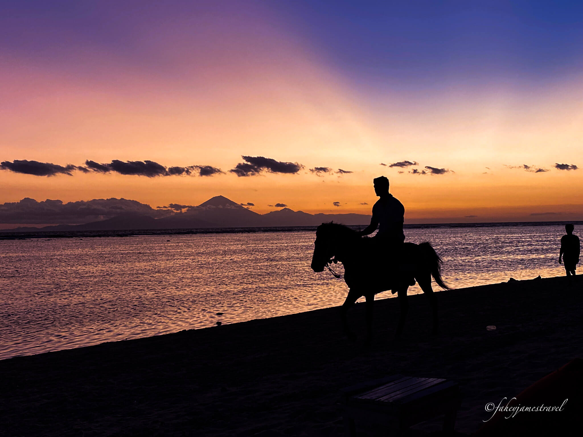 a man rides a horse along sunset beach on gili trawangan
