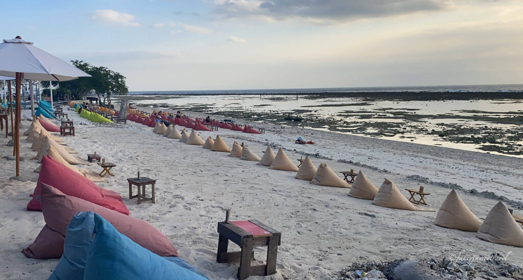 beans bagssit on thw sand around gili t. the sky is cloudy and the un is setting