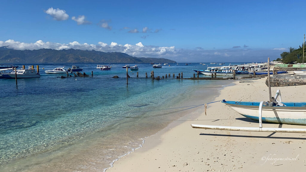 some boats sit on the white sands of gili t with water to the left being crystal clear 