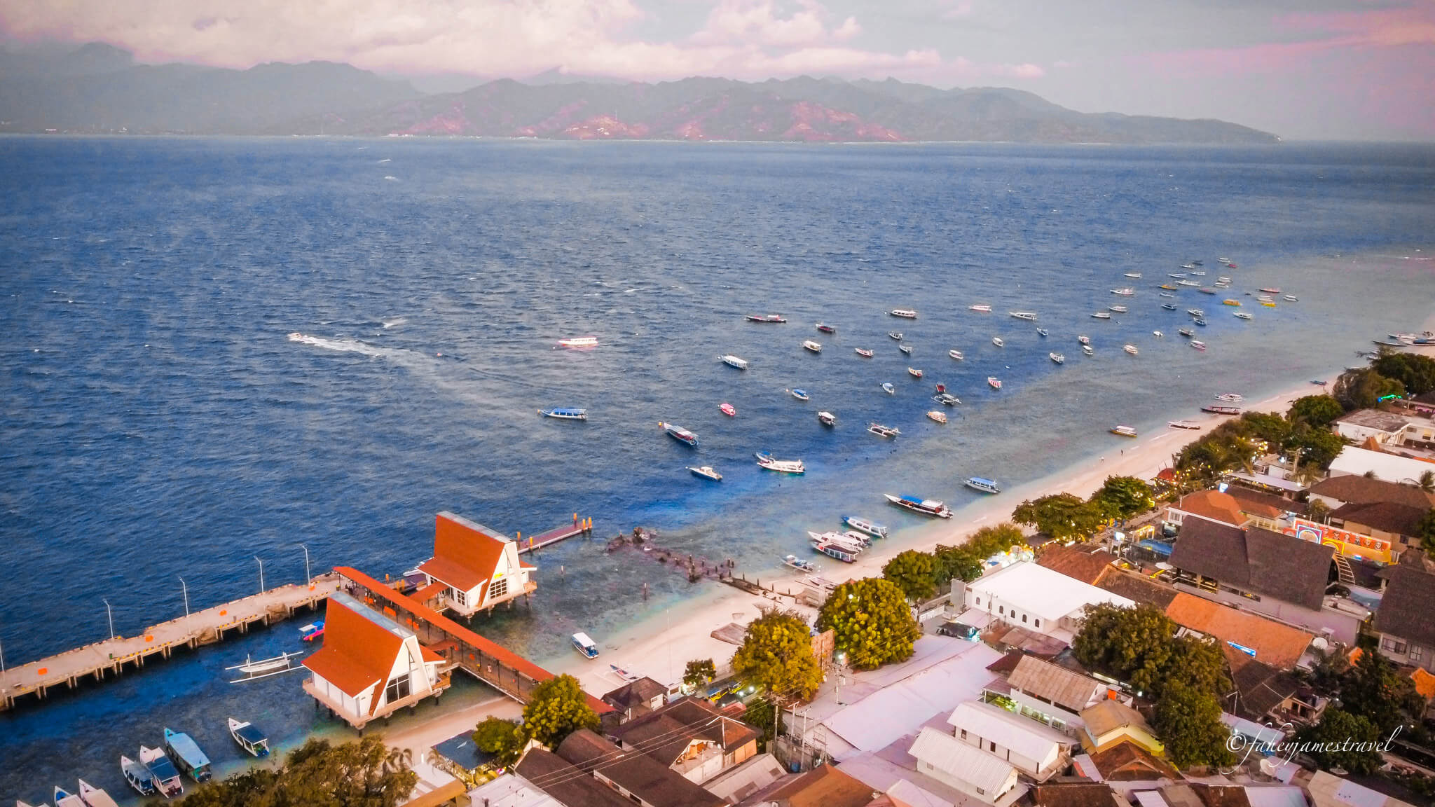 the pier is visible in the foreground and gili meno and gili air are visible in the background. Its a drone shot from about 100 metres