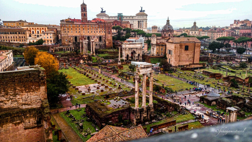 an shot of the roman forum in rome from high above looking down on the green grass and ruins
