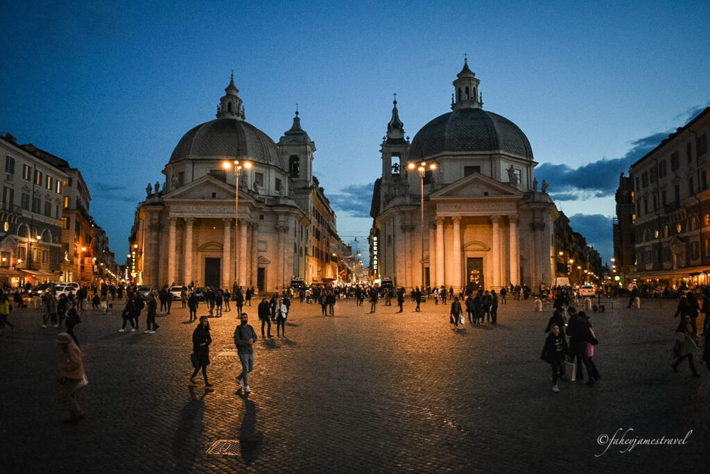 two churches stand side by side beside Piazza del Popolo and people fill the streets as the sun sets