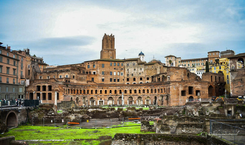 a shot inside the roman forum. some green grass in the foreground and a cloudy sky 