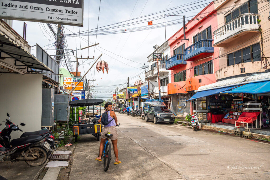 guada sits on a bike and turn to james who takes a photo of her from behind. there are tall apartments on the right side