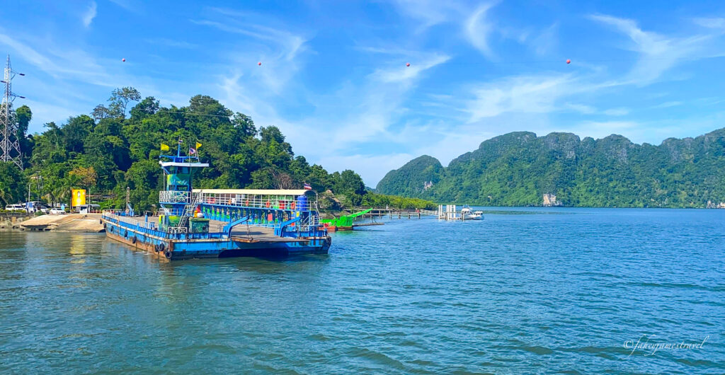 car ferry is shown at the pier at Hua Hin pier close to koh lanta. The water is blue as is the sky. there are karst limestone cliffs in the background