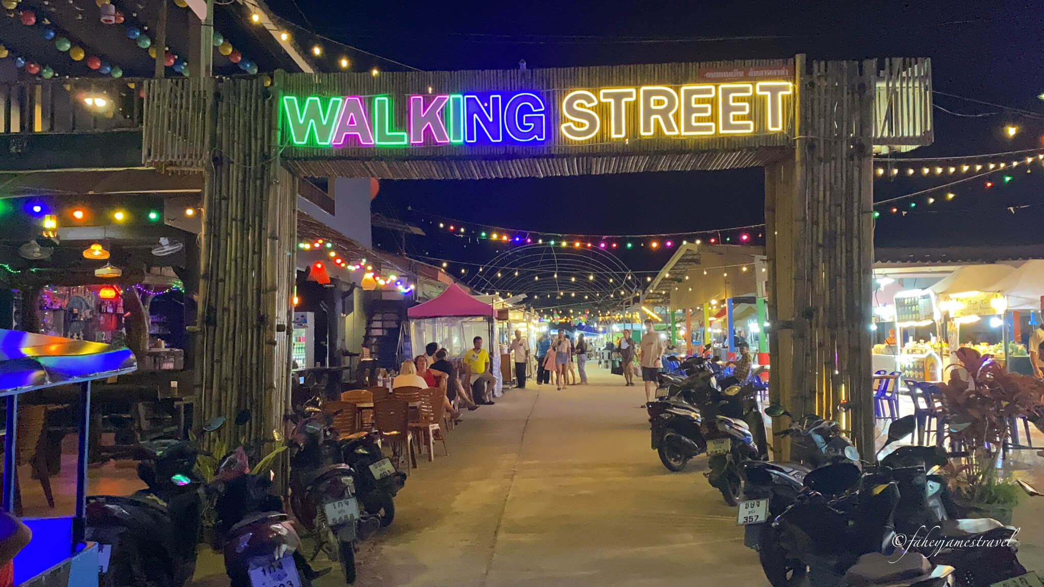 the entrance to koh lanta night market walking street is shown. the lights are green, blue and yellow