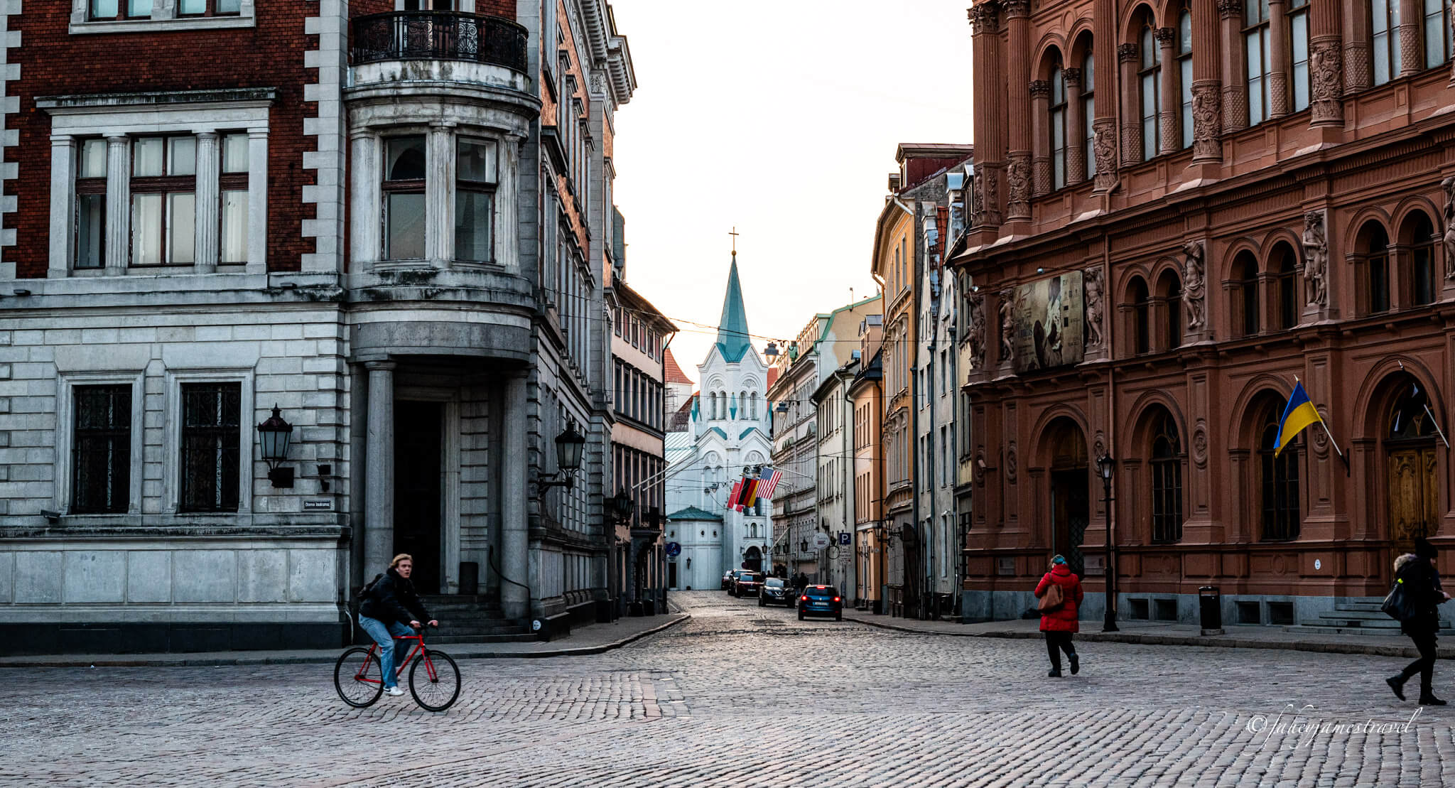 A woman rides a bike through Riga's old town with a church in the background during March