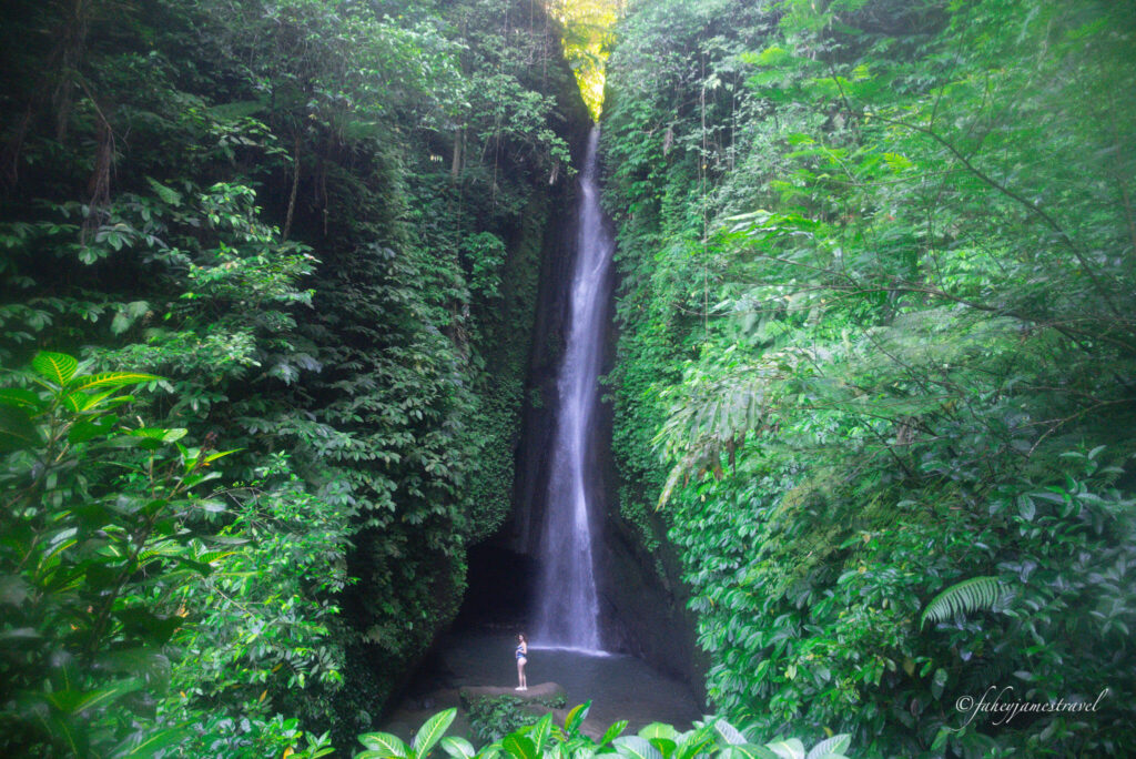 a girl stands at the bottom of the waterfall