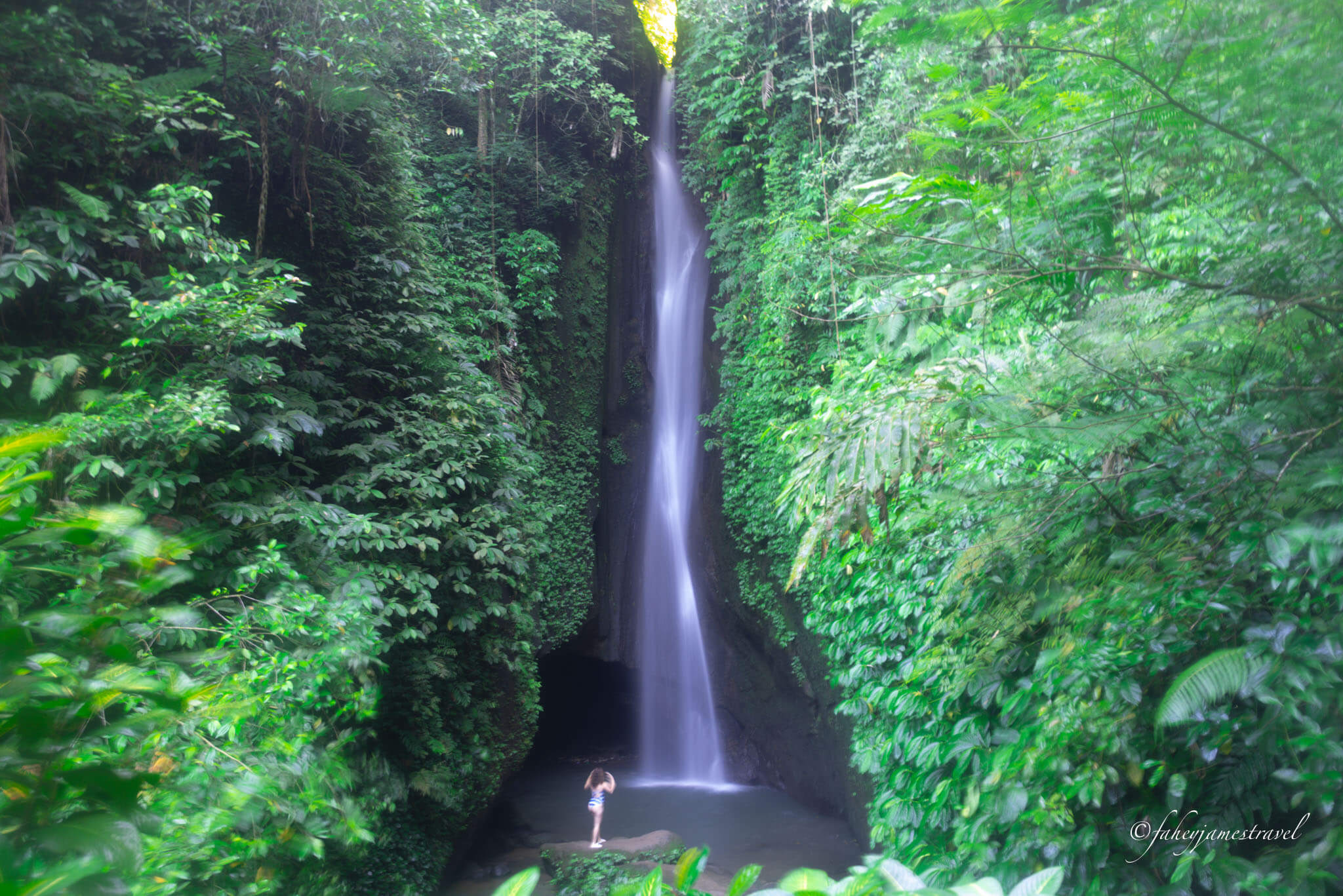 leke leke waterfall is shwon with soembody standing right at the bottom with green leaves all around
