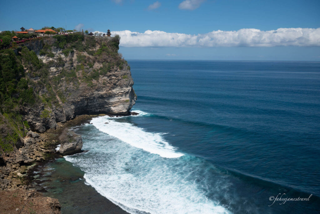 uluwatu beach in bali is pictured with waves crashing below with a blue sky