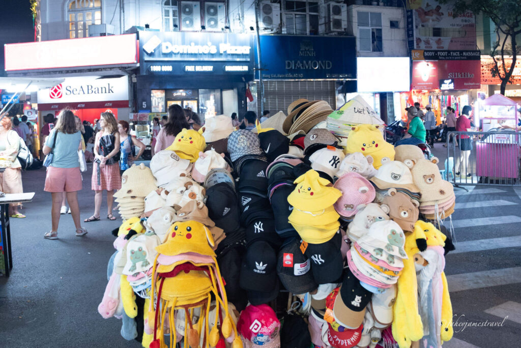 a lady is holding lots of clothes at hanoi night market in the middle of the street