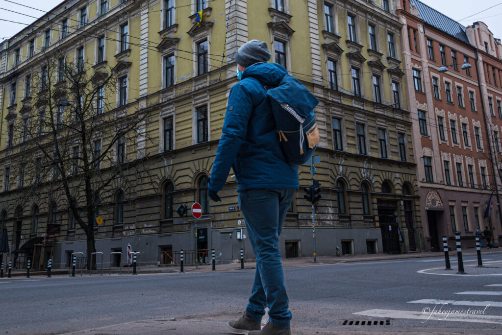 james stands at a crossroads in latvia with the street colourful green behind