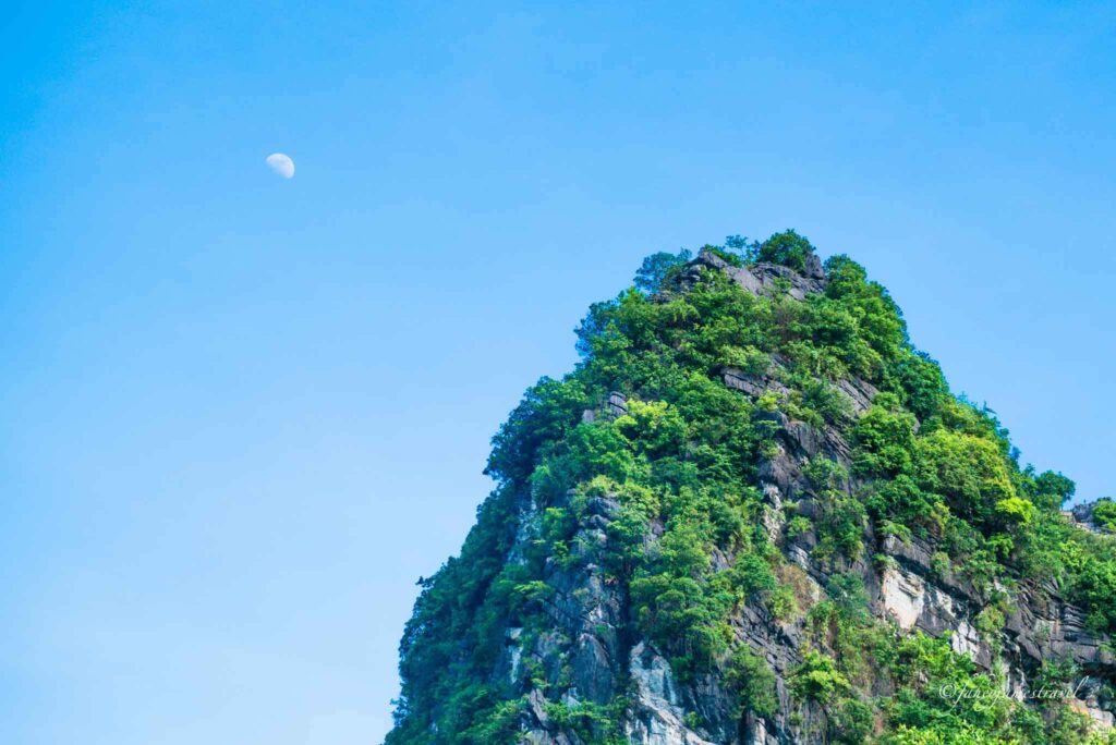 limestone cliff and the moon is pictured in tam coc